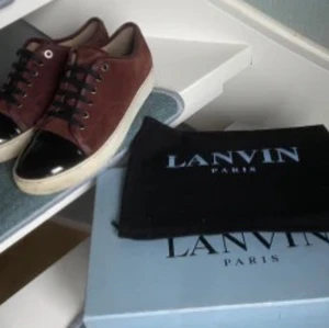 Bruna sneakers från Lanvin - Snygga bruna sneakers från Lanvin med svart tå och vita sulor. Skorna har snörning och en stilren design som passar perfekt för en trendig look.