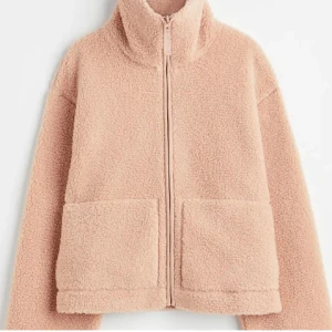 Beige teddyjacka med dragkedja - Mysig beige / rosa teddyjacka med dragkedja och stora fickor framtill. Perfekt för kyliga dagar med sin fluffiga och varma design. Jackan har en hög krage och långa ärmar för extra komfort. Pris kan diskuteras 