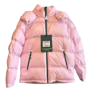 Rosa dunjacka från Moncler - Säljer en snygg limited edition rosa dunjacka från Moncler x FRGMT med huva och dragkedjor. Jackan har en puffig design och är perfekt för kyliga dagar. Den har en stilren look med Moncler-logga på insidan.