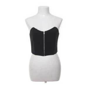 Svart korset topp med dragkedja - Snygg svart tubtopp med dragkedja framtill. Perfekt för en stilren look. Passar bra till både jeans och kjol.