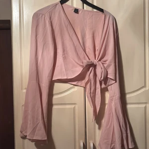 Rosa knytblus från Shein - Säljer en söt rosa blus från Shein med knytning framtill. Blusen har långa ärmar med volangdetaljer som ger en romantisk känsla. Perfekt för en stilfull look.