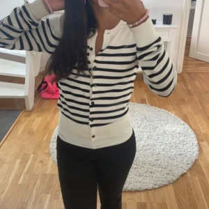 Randig kofta i svart och vit - Säljer en stilren randig kofta i svart och vit med knappar framtill. Perfekt för en avslappnad look. Koftan har långa ärmar och en bekväm passform. Passar bra till både jeans och kjol.