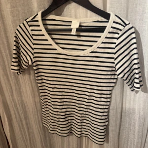 Randig topp från H&M - Säljer en randig topp från H&M i svart och vit. Toppen har korta ärmar och en rund halsringning. Perfekt för en avslappnad stil.