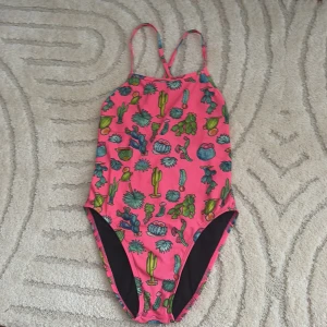 Rosa baddräkt med kaktusmönster från Jolyn - Snygg rosa baddräkt från Jolyn med coolt kaktusmönster. Perfekt för träningen.Tillverkad i 100% polyester för en skön passform och hållbarhet. Är i storlek 26 men den är lite större. Den är väl andvänd med lite knottror på rumpan. Nypris 800 säljs för 150 kr . Pris kan diskuteras.