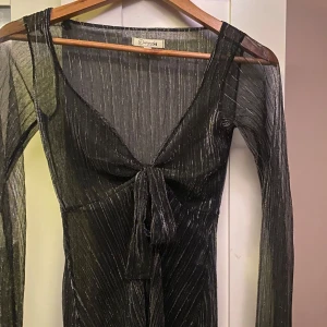 Glittertopp från Design by Si - Snygg svart glittrig topp från Design by Si i storlek XS. Toppen har en v-ringad design med knytning framtill och långa ärmar. Perfekt för en kväll ute med vänner! ✨ Endast testad men aldrig använd:) Kontakta mig för frågor, bilder eller prisförslag🩷