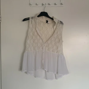 Vit spetsblus från H&M Divided - Säljer en söt vit blus från H&M Divided. Den är ärmlös med spetsdetaljer och knappar framtill. Perfekt för en somrig look med sin luftiga design och vackra spetsmönster. Passar bra till både jeans och kjol!