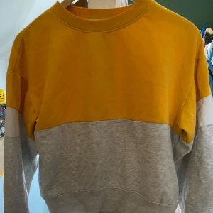 Gul och grå sweatshirt - Säljer en cool sweatshirt i gult och grått med vita detaljer. Tröjan har en avslappnad passform och långa ärmar. Passar perfekt för storlek XS även om det är barn storlek 152
