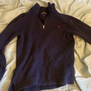 Mörkblå tröja från Polo Ralph Lauren - Säljer en stilren mörkblå tröja från Polo Ralph Lauren med en liten röd logga på bröstet. Tröjan har en dragkedja vid halsen och långa ärmar. Perfekt för en avslappnad och snygg look.
