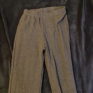 Grå ribbade byxor med matchande tröja - Säljer ett par grå ribbade byxor med loose passform. Byxorna har en elastisk midja för extra komfort och är perfekta för en avslappnad stil. De är tillverkade i ett mjukt material som känns skönt mot huden.