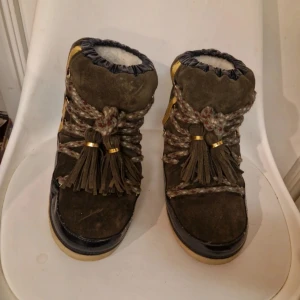 Bruna mocka boots med fransar - Snygga bruna boots i mocka med fransar och snörning. De har en mysig pälsfodring som gör dem perfekta för kyligare dagar. Skorna har en robust sula och dekorativa detaljer i guld.