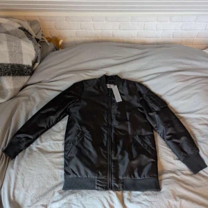 Svart bomberjacka från Calvin Klein - Ny pris 2800.                                      Helt oanvänd pågrund av att den varit för stor. Dags att sälja!!Snygg svart bomberjacka från Calvin Klein med quiltad insida och dragkedja framtill. Jackan har ribbade muddar och en broderad logga på ryggen. Perfekt för en stilren look. 