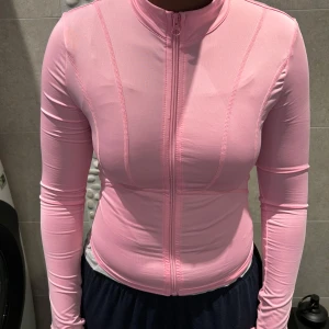 Liknande lululemon tröja - Säljer en rosa långärmad träningströja med dragkedja framtill. Tröjan har en tight passform och är tillverkad i ett syntetmaterial som andas. Perfekt för träning och andra aktiviteter. Den har även tumhål vid ärmsluten för extra komfort.