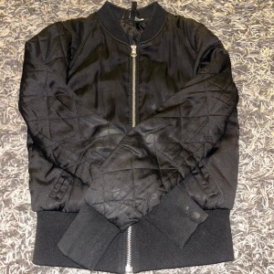 Svart bomberjacka från H&M  - Snygg svart bomberjacka från H&M med dragkedja framtill. Dragkedjan har tappat lite färg men inget man tänker på. Finns också en fläck på ena ärmen, men går troligtvis bort i tvätten!
