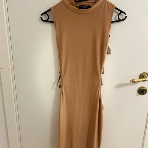 Beige ärmlös klänning med snörning på sidorna - Snygg beige klänning i ett mjukt material med ärmlös design och snörning på sidorna. Perfekt för en utgång