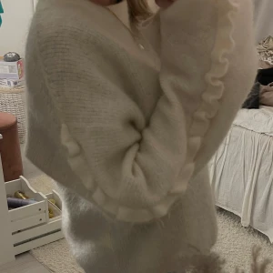 Vit stickad tröja med volanger - Vit stickad tröja med volangdetaljer på armarna, mohair och ull blandning