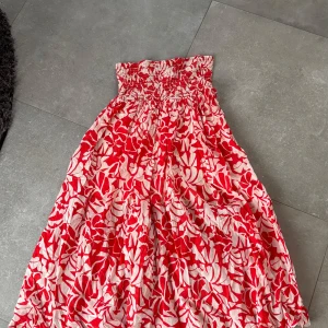 Röd och vit blommig långkjol - Säljer en härlig röd och vit långkjol med blommigt mönster. Kjolen har en elastisk midja som ger en bekväm passform. Perfekt för sommarens varma dagar!