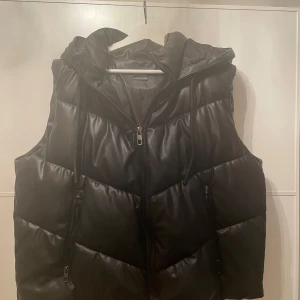 Svart dunväst från Zara - Snygg svart dunväst från Zara med dragkedja och huva. I skinn material. Använd men i mycket bra skick