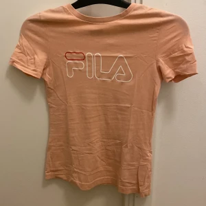 Rosa t-shirt från FILA - Snygg rosa t-shirt från FILA med deras ikoniska logga i vitt och rött på bröstet. Perfekt för en avslappnad stil. 