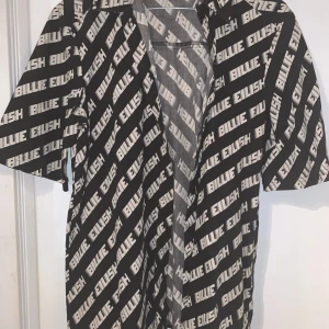 Svart och vit skjorta från H&M Divided - Cool skjorta från H&M Divided med svart och vit design och texten 'Billie Eilish' över hela plagget. Skjortan har korta ärmar och en avslappnad passform. Perfekt för fans av Billie Eilish! Står xxs men det passar för större storlek. Hör av dig vid frågor😊