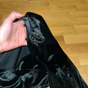Svart sammetstopp från BikBok - Snygg svart topp i sammet från BikBok med långa ärmar och en elegant v-ringad design. Perfekt för en stilfull look med en touch av glamour.