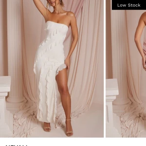 Vit axelbandslös klänning - Elegant vit axelbandslös klänning med volangdetaljer och asymmetrisk slits. Använd en gång. Köpt för 1200. Pris går att diskutera. Perfekt för balen. KÖP INTE UTAN ATT KONTAKTA MIG! 