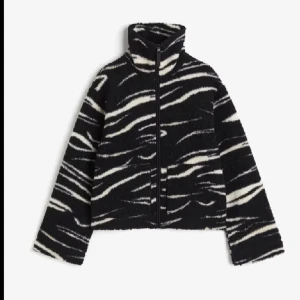 Svart och vit teddyjacka med zebramönster - Snygg och trendig teddyjacka i svart och vitt med zebramönster. Jackan har en dragkedja framtill och hög krage för extra värme. Super fint skick!