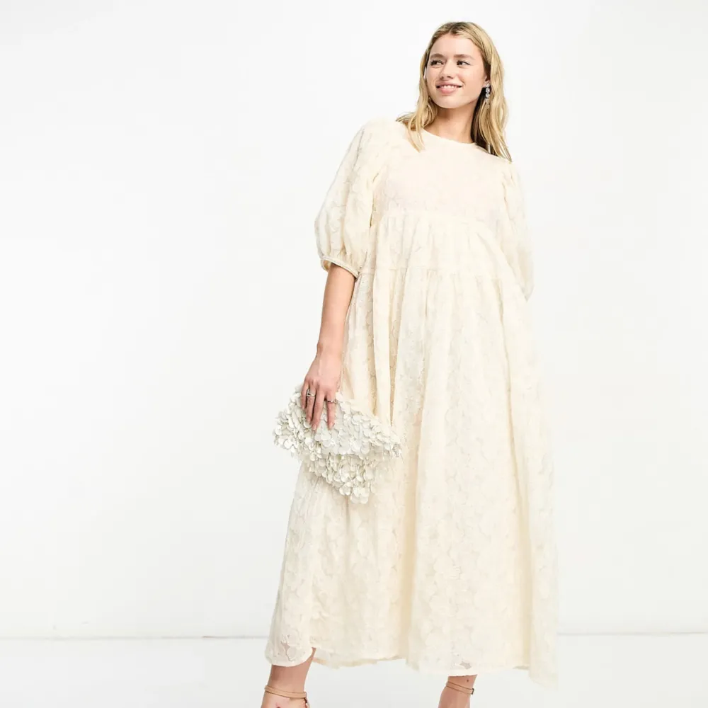 Säljer en elegant champagnefärgad långklänning med ett vackert blommigt mönster. Klänningen har puffiga trekvartsärmar och en luftig passform som ger en somrig, söt vibe. Perfekt för speciella tillfällen såsom studenten/midsommar. Den är helt ny med prislapp. Dream Sister Jane. Ärmarna har insydda pärlor. . Mekot.