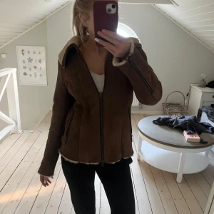 Brun mockajacka från Hunkydory - Säljer en snygg brun mockajacka från Hunkydory med mysigt foder i pälsimitation. Jackan har dragkedja och långa ärmar, perfekt för kyligare dagar. Den har en klassisk look med en modern twist. Passar perfekt för höst och vinter. Nypris 10000kr