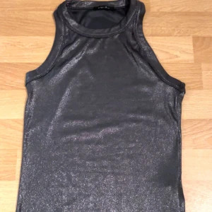 Svart glittrig linnetopp - Snygg svart glittrig linnetopp i ett stretchigt material. Perfekt för en kväll ute eller när du vill glittra lite extra. Toppen är ärmlös och har en rund halsringning. Från New Yorker. 