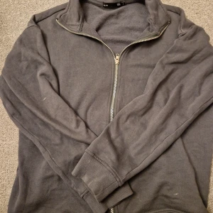 Mörkgrå hoodie med dragkedja - Säljer en mörkgrå hoodie med dragkedja. Tröjan har långa ärmar och en hög krage. Perfekt för kyliga dagar. Hör av dig vid intresse!