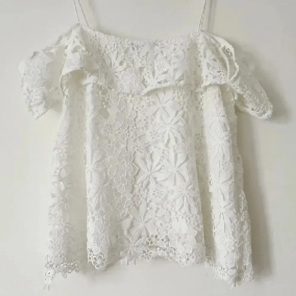 Säljer en söt vit spetsblus med offshoulder-design och korta ärmar. Blusen har ett vackert blommigt mönster och tunna axelband. Perfekt för sommarens varma dagar.. Yläosat.