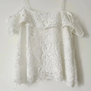 Vit spetsblus - Säljer en söt vit spetsblus med offshoulder-design och korta ärmar. Blusen har ett vackert blommigt mönster och tunna axelband. Perfekt för sommarens varma dagar.