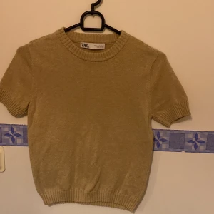 Beige kortärmad tröja från Zara - Säljer en stilren beige stickad  tröja från Zara med korta ärmar och rund hals. Tröjan har ribbade kanter vid ärmslut och nederkant, vilket ger en snygg passform. Perfekt för en avslappnad look. Storlek s men passar även xs
