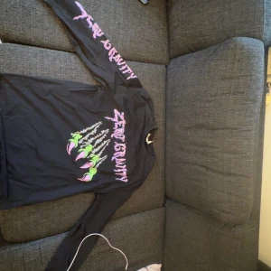 Svart långärmad tröja från Weekday - Säljer en svart långärmad tröja från Weekday med trycket 'Zero Gravity' i rosa och grönt. Tröjan har ett coolt motiv av klor på framsidan och text på ärmarna. Perfekt för en avslappnad stil. Oversized fit, använd 1 gång