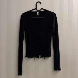 Nelly Topp - Topp från Nelly. Stretchigt, ribbat material. Långa ärmar med en volangkant vid ärmsluten. Tre knytdetaljer mellan byst. V-formad halsringning.  