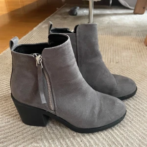 Grå boots med dragkedja - Säljer ett par snygga grå boots i mocka med dragkedja på sidan. De har en bekväm klack och är perfekta för höst och vår. Skorna är i bra skick och passar både till vardags och fest. Storleken är dam 38.