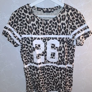 Leopardmönstrad t-shirt  - Cool leopardmönstrad t-shirt från Happy Holly i storlek 36/38. Den har korta ärmar med vita ränder och ett stort tryck med siffran 26 på framsidan. Perfekt för en avslappnad och trendig look! Nästan aldrig använd😊✨️