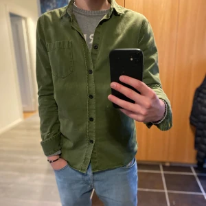 Grön skjorta från Nudie Jeans - Säljer en snygg grön skjorta från Nudie Jeans i storlek S. Skjortan är gjord av 100% ekologisk bomull och har en klassisk krage med knappar!👍🤝😃
