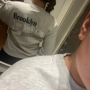 Grå sweatshirt med tryck - Säljer en snygg grå sweatshirt med tryck av 'Brooklyn New York City' på ryggen och 'NYC Brooklyn' på framsidan. Perfekt för en casual look och superbekväm att ha på sig. Passar bra till både jeans och leggings. 