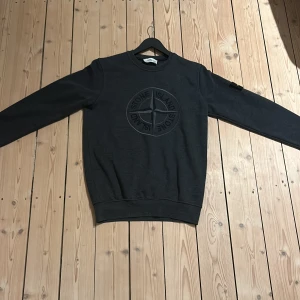 Mörkgrå sweatshirt från Stone Island - Säljer en snygg mörkgrå sweatshirt från Stone Island i mycket bra skick. Tröjan har en rund halsringning och det ikoniska Stone Island-märket på ärmen. Perfekt för höst och vår, och passar både till vardags och lite mer avslappnade tillfällen. Strlk M passar också S