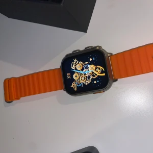 Smartwatch med orange armband - Säljer en Philippe Palmer smartwatch med ett coolt orange armband. Klockan har en fyrkantig display med en snygg urtavla. Perfekt för dig som vill ha en stilren och modern accessoar. Laddare och originalförpackning ingår. Nypris på ca 1800kr. Pris kan diskuteras