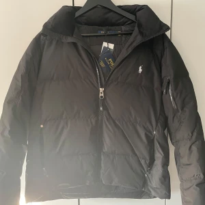 Svart dunjacka från Ralph Lauren - Säljer en snygg svart dunjacka från Ralph Lauren i helt nytt skick med alla tags. Jackan har en dragkedja framtill och en liten logga på bröstet. Perfekt för kalla dagar med sin varma och bekväma passform. Hör av dig om du har några frågor eller sånt! Pris inte hugget i sten.