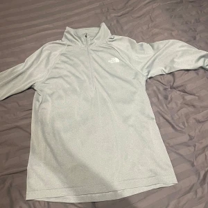 Grå tröja från The North Face - Säljer en grå tröja från The North Face i mycket bra skick. Den har en halv dragkedja och är perfekt för kyligare dagar. Tröjan är bekväm och stilren, idealisk för både vardag och utomhusaktiviteter. Passar perfekt för höst och vår!