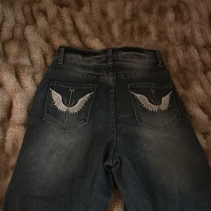 Blå jeans med broderade fickor - Säljer ett par snygga blå jeans med coola broderade vingar på bakfickorna. . Jeansen är i bra skick och passar perfekt till både vardag och fest. Sköna och stiliga, ett måste i garderoben! 💙