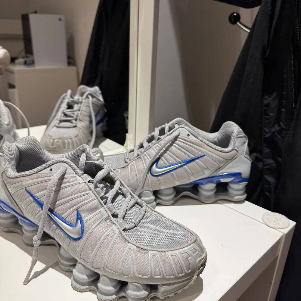 Säljer ett par grå Nike Shox sneakers i mycket bra skick. De har en cool design med blå detaljer och den ikoniska Shox-sulan som ger extra studs i steget. Perfekta för både träning och vardag. Storlek passar de flesta med normal passform.. Skor.