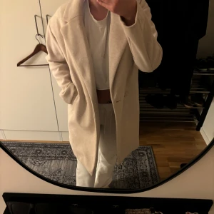 Beige kappa från Pull&Bear - Säljer en superfin beige kappa från Pull&Bear i storlek XS. Den har en klassisk design med knappar framtill och är perfekt för höst och vår. Materialet känns mjukt och bekvämt, vilket gör den idealisk för både vardag och fest. Passar perfekt till alla outfits! Inga skador på jackan alls då den är använd endast 1 gång!