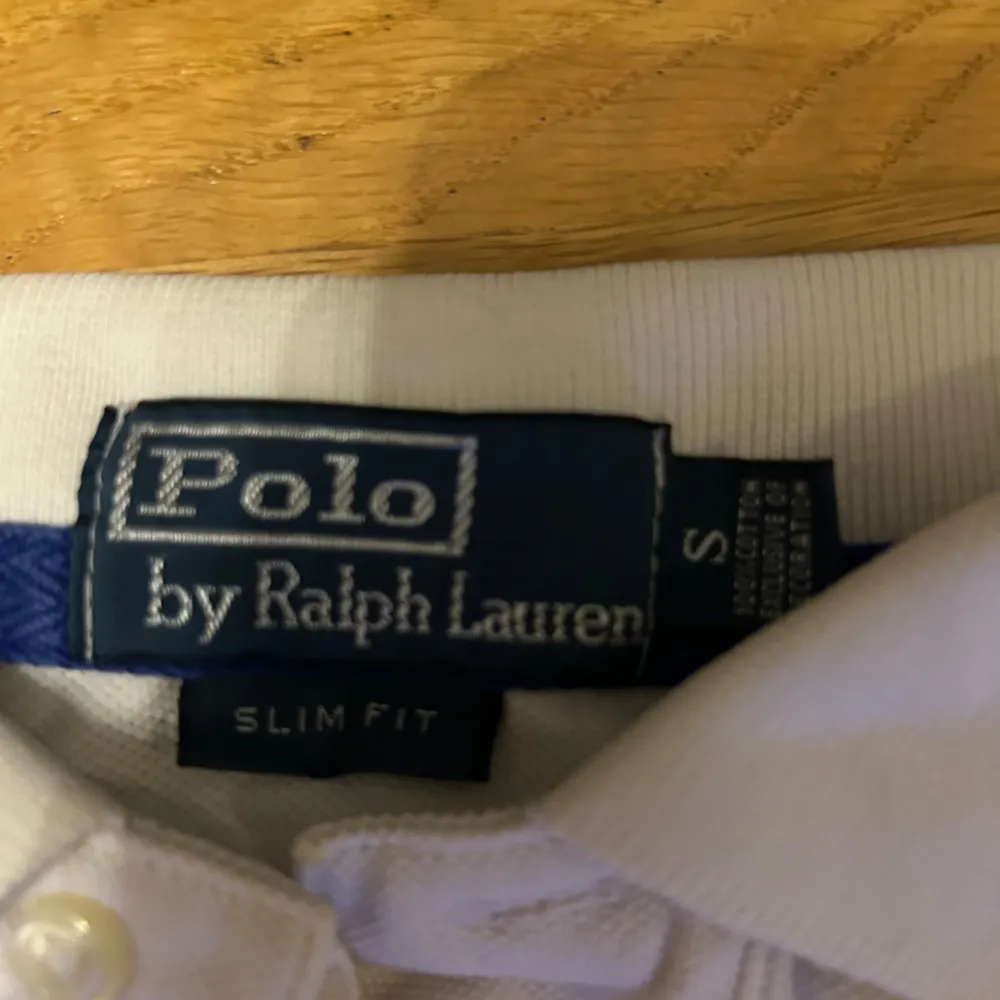 Säljer en klassisk vit pikétröja från Ralph Lauren i slim fit. Den har en broderad blå logga på bröstet och knappar vid kragen. . T-shirts.