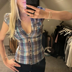 Rutig blus med korta ärmar - Säljer en superfin rutig blus i blå, lila och beige toner. Den har korta ärmar och knappar hela vägen ner samt ett knytband i ryggen💗Skulle nog passa xs-m eftersom det går att knyta bak i midjan och justera storleken.