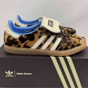 Adidas x Wales Bonner sneakers med leopardmönster - Supercoola Adidas x Wales Bonner sneakers i leopardmönster! De har en unik design med pälsliknande yta och klassiska vita ränder. Insidan är klädd i en fräsch blå färg och de har en bekväm gummisula. Perfekta för att sticka ut i mängden!