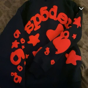 Sp5der hoodie äkta finns kvitto o allt  - Säljer en cool mörkblå hoodie med röda tryck i form av stjärnor och hjärtan. Perfekt för att sticka ut i mängden! Den har en bekväm passform och är perfekt för både höst och vinter. Passar lika bra till skolan som till en chill dag hemma.
